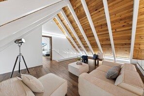 Ein modernes Schlafzimmer im Loft-Stil mit schrägem Dach, Holzbalken, einem großen Fenster und einer gemütlichen Sitzecke mit Kissen.
