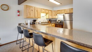 A kitchen with wooden cabinets, a stainless steel refrigerator, a granite countertop, and two bar stools. - Summer Fun! Winter Park Condo w/ Pool, Hot Tub (Winter Park)