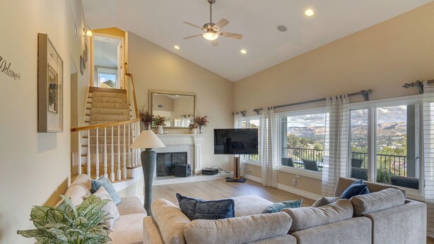 A spacious living room with a large sectional sofa, a flat-screen TV, a fireplace, and a balcony with a view.