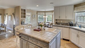 A kitchen with white cabinets, a large island with a sink, and a dining area with chairs and a table.