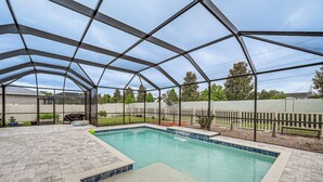 Una piscina con patio a motivi a spina di pesce, circondata da una struttura in copertura metallica.