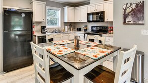 Une cuisine moderne avec des meubles blancs, un réfrigérateur noir, des appareils en acier inoxydable et une table à manger avec des sets de table.
