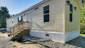 Une maison mobile de plain-pied, dotée d’un porche à l’avant, d’un escalier et d’une petite fenêtre.
