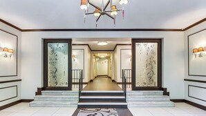 Eine Hotelhalle mit einer zentralen Treppe, dekorativen Wandverkleidungen und einem Kronleuchter.