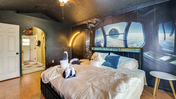 A bedroom with a large bed, a ceiling fan, a view through a window, and a small table. - Themed Interior, Poolside Fun! Villa Near Disney (Davenport)