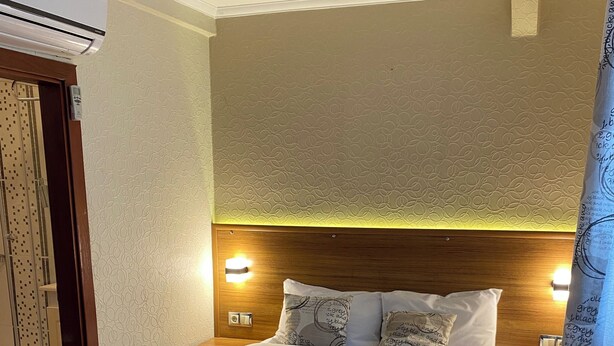 A neatly made bed with a quilt, pillows with text, bedside lamps, and a wall-mounted air conditioner. - KAAN AİLE PANSİYON (Amasra)