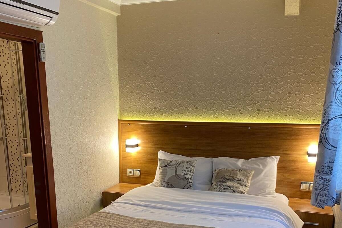 Una habitación de hotel con una cama grande, dos mesitas de noche, aire acondicionado de pared y una cortina.