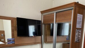 A room with a TV, a wooden cabinet with a mirror, a trash can, and a sofa. - KAAN AİLE PANSİYON (Amasra)
