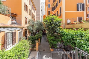 A narrow alleyway between buildings with balconies, potted plants, and a small gate. - Blue River Trastevere (Rome)