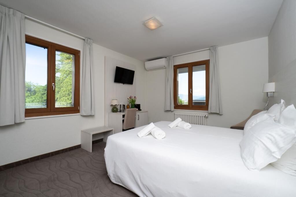 A hotel room with a bed, a desk, a television, and windows with curtains.