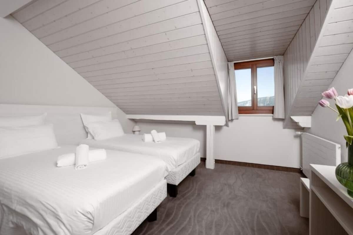 A bedroom with two beds, a window, and a wooden ceiling.