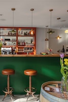 Uma área de bar com banquetas, balcão e prateleiras com garrafas.