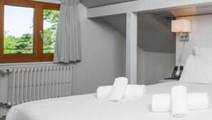 A hotel room with a large bed, a window with curtains, a radiator, and a bedside lamp.
