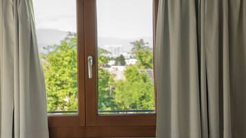 Ein Hotelzimmer mit Bett, einem Fenster mit Vorhängen und Blick auf Grünflächen und Gebäude.