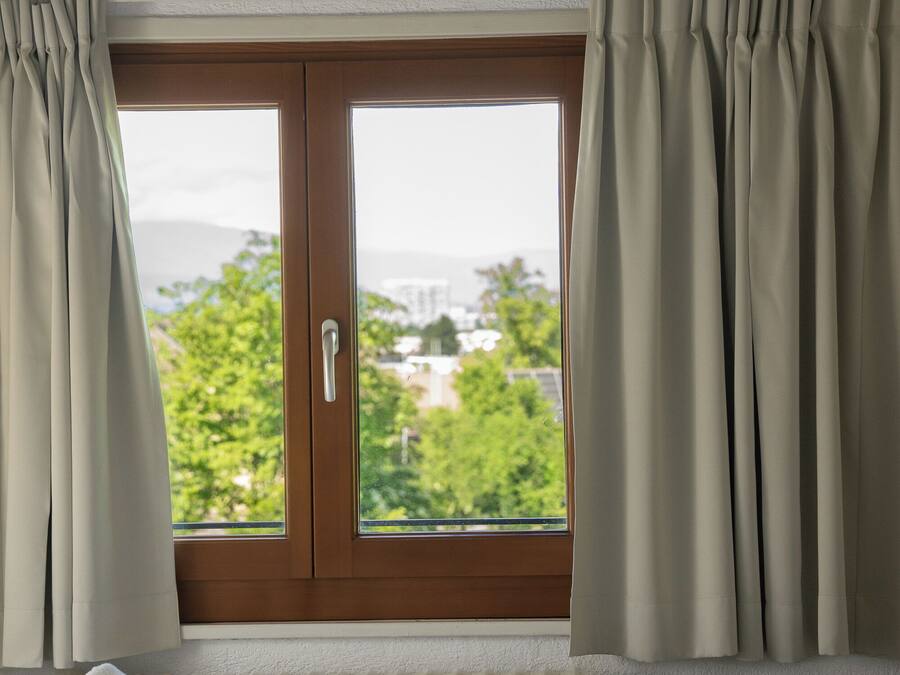 Ein Hotelzimmer mit Bett, einem Fenster mit Vorhängen und Blick auf Grünflächen und Gebäude.