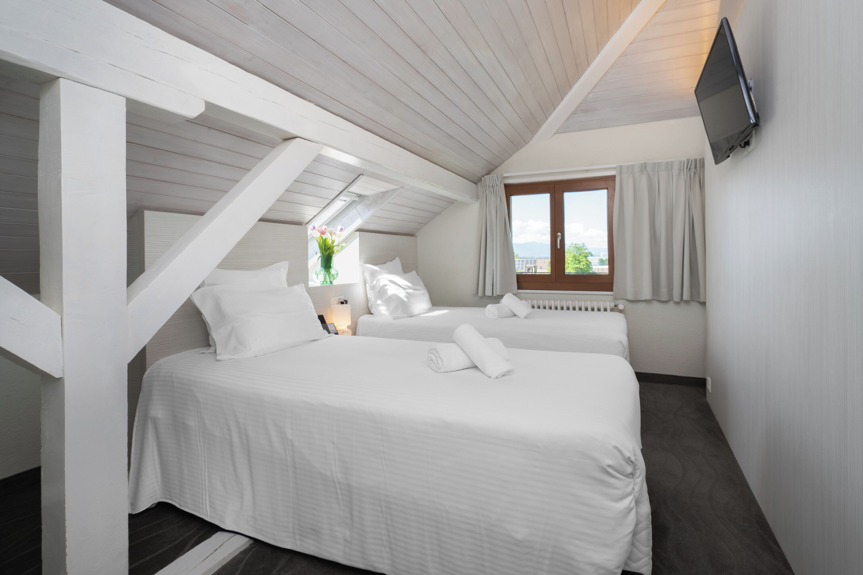 Ein Schlafzimmer mit zwei Betten, einem an der Wand montierten Fernseher und einem Fenster mit Vorhängen.