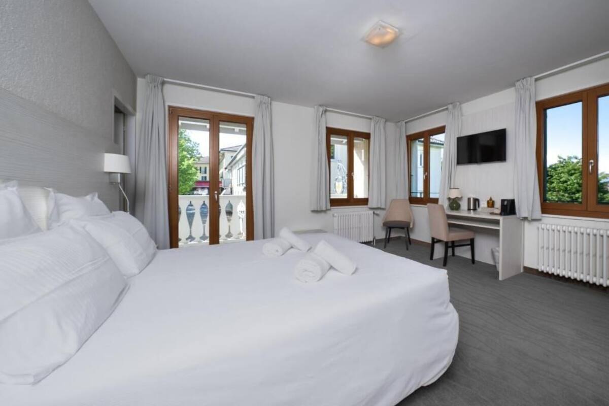 A hotel room with a large bed, a desk, a chair, a TV, and a view of the outside.