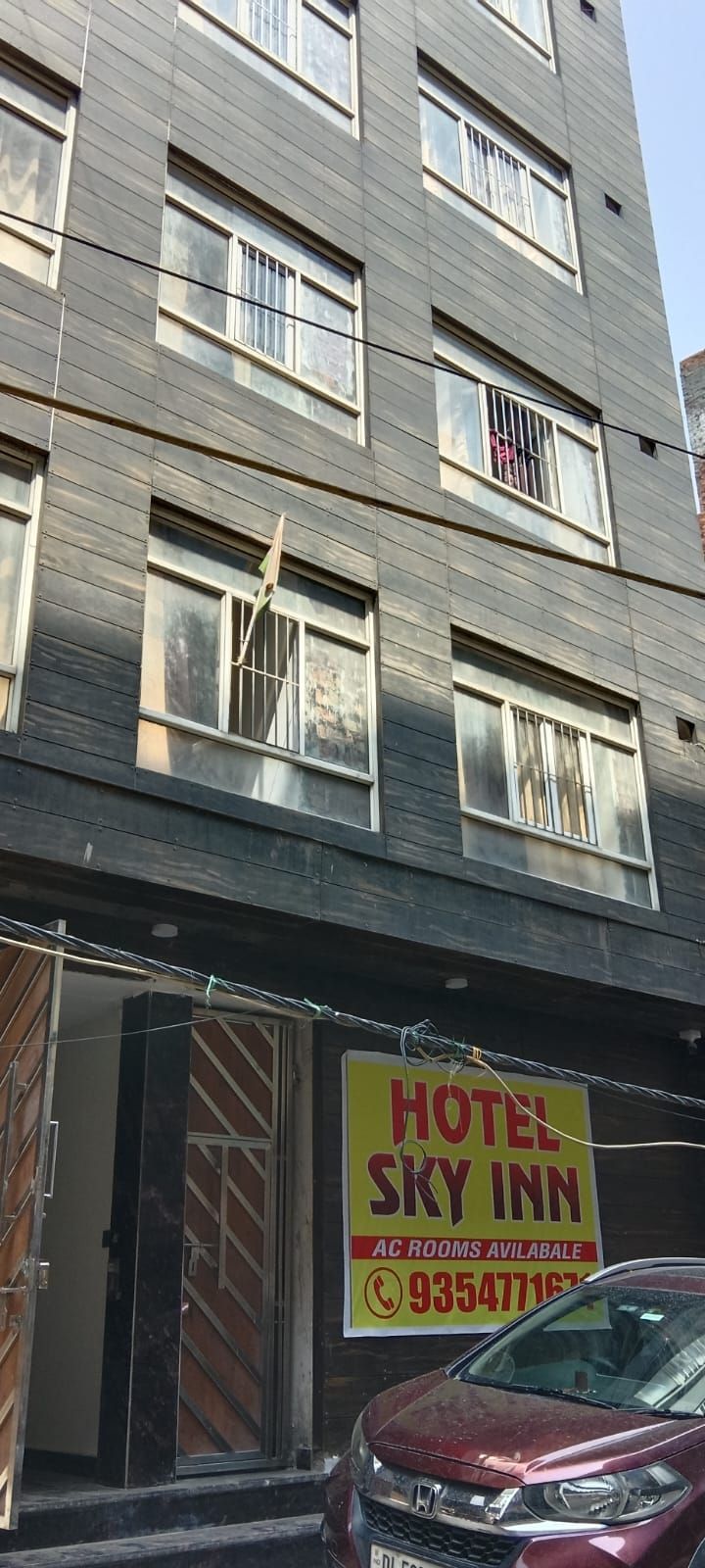 A multi-story building with a sign for 'Hotel Sky Inn' advertising available AC rooms.