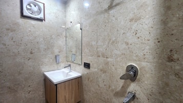 Een badkamer met een marmeren wand, een houten wastafelmeubel, een spiegel, een wandwastafel en bediening voor de douche.