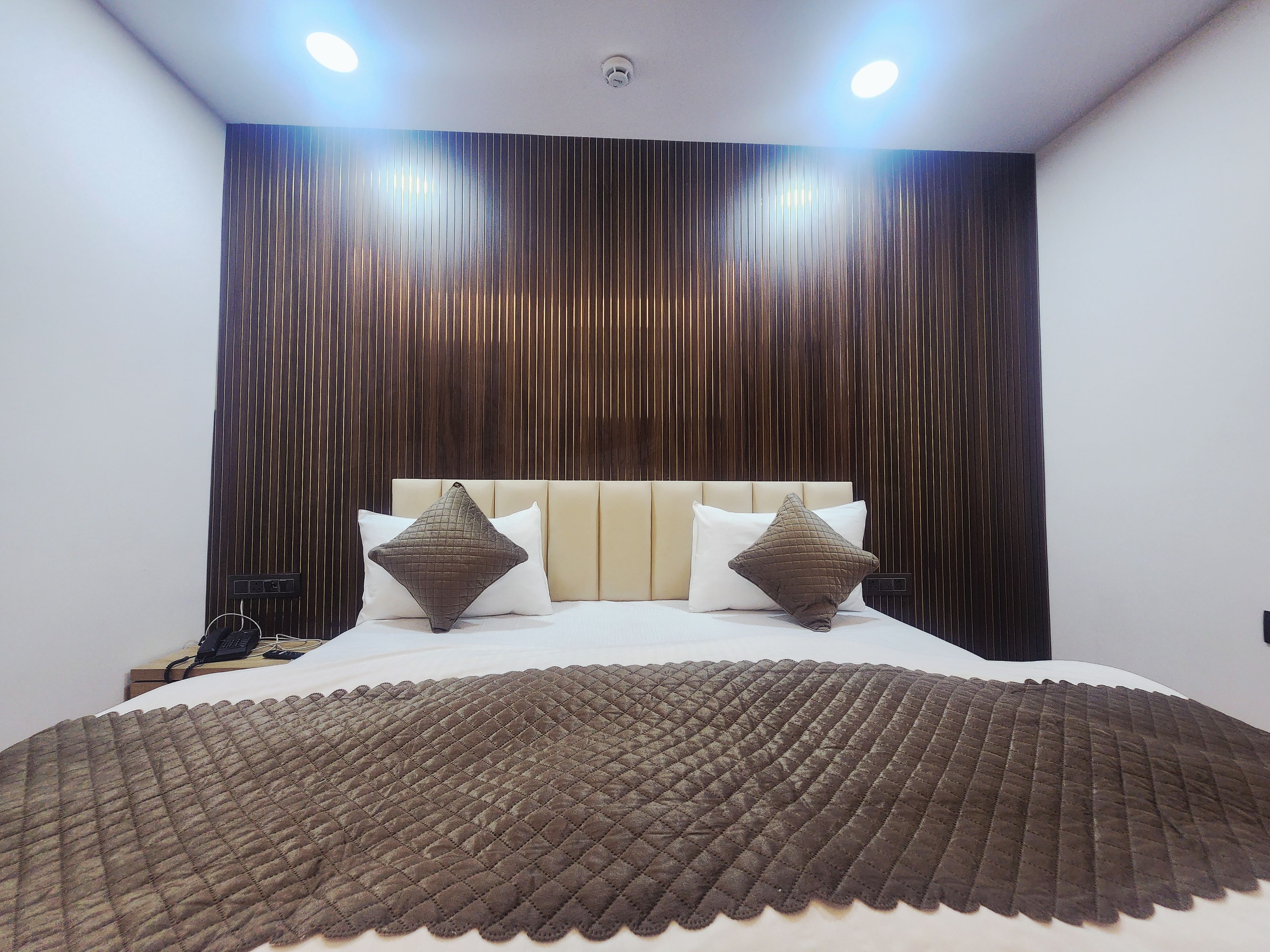 A hotel room with a bed, two pillows, a headboard, and a wall with vertical lines.