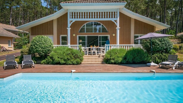 Ein Poolbereich mit Holzterrasse, Liegestühlen und einer überdachten Terrasse.
