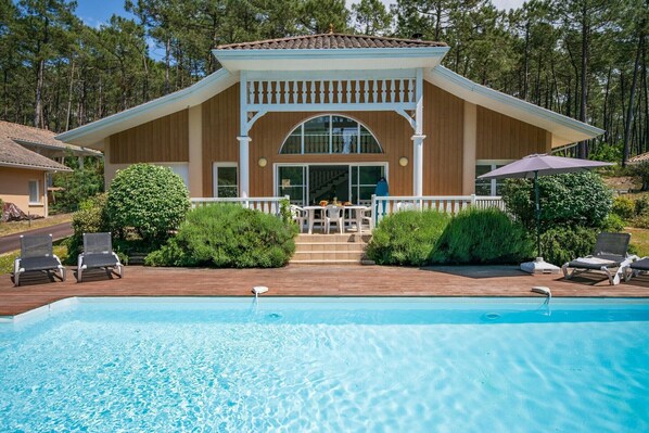 A poolside area with a wooden deck, lounge chairs, and a covered patio.