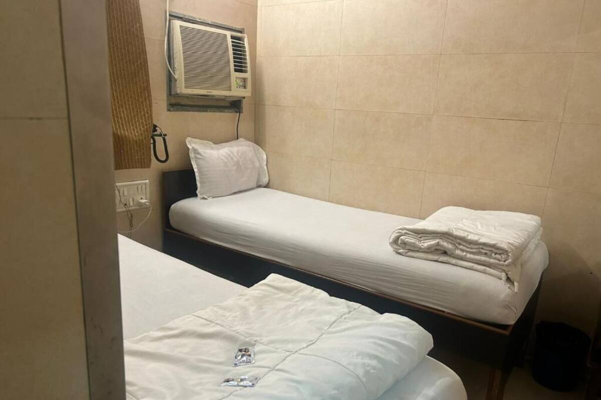 Una habitación pequeña con dos camas, aire acondicionado de pared y un enchufe a la vista.