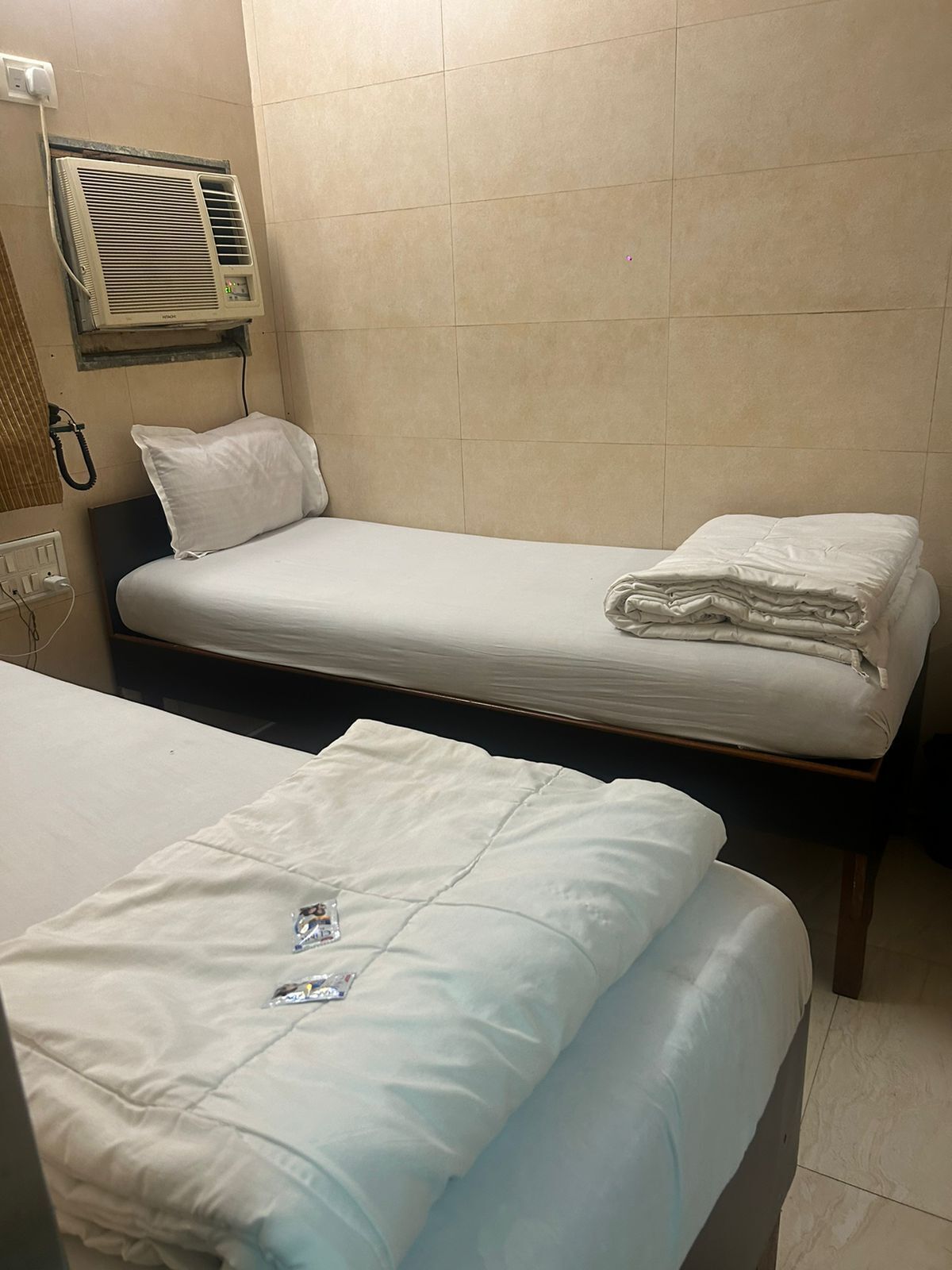 A hotel room with two single beds, a wall-mounted air conditioner, and a bedside telephone.