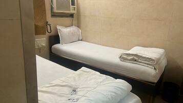 Una habitación pequeña de hotel con dos camas individuales, aire acondicionado instalado en la pared y un teléfono.