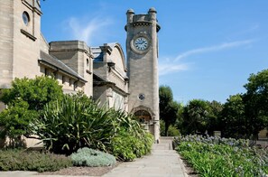 A historic building with a clock tower, a stone facade, and a garden with various plants. - Bright 1BDR Flat between Forest Hill East Dulwich (Greater London)