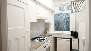 A kitchen with white cabinets, a gas stove, a sink, and a window with a view of trees. - Bright 1BDR Flat between Forest Hill East Dulwich (Greater London)
