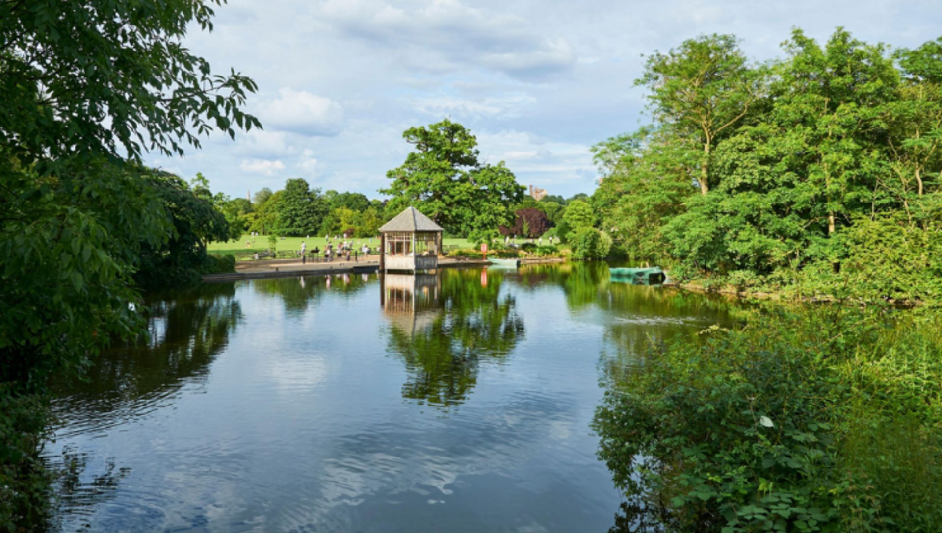 A tranquil lake with a gazebo and a boat dock, surrounded by lush greenery.