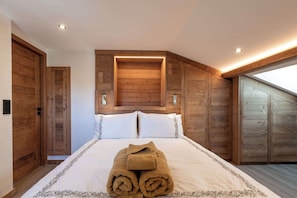 Ein Schlafzimmer mit Holzboden, Oberlicht und einem Bett mit weißen Leinen. Ein gerolltes Handtuch liegt auf dem Bett.