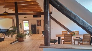A spacious loft with exposed wooden beams, a dining area with a table and chairs, and a large potted plant.