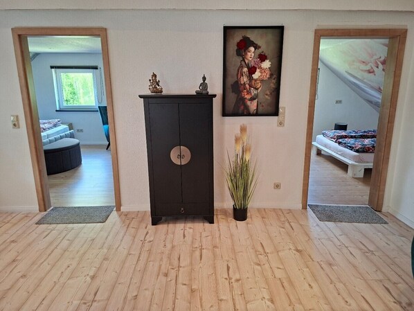 A room with a wooden floor, a dark cabinet with a circular lock, a painting of a woman holding flowers, and a bed with a floral bedspread.
