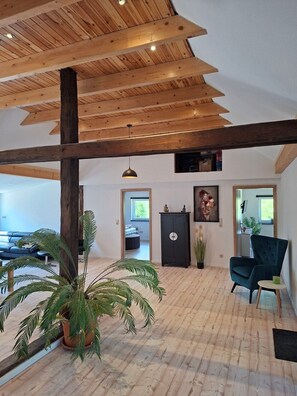 A spacious room with wooden beams, a sofa, a chair, and potted plants.