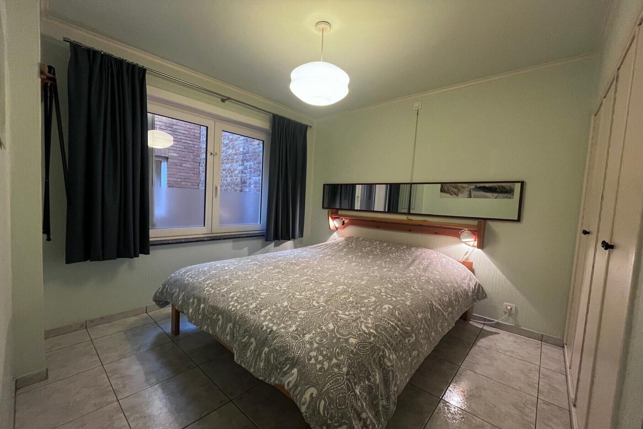 A bedroom with a bed, a window with curtains, a bedside lamp, and a wall-mounted picture.