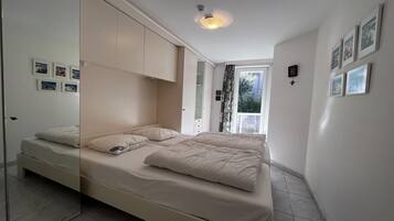 Een slaapkamer met een bed, een kledingkast, een raam en foto’s aan de muur.