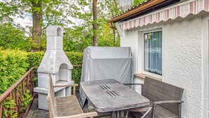 Eine Terrasse im Freien mit einem Grill aus Naturstein, einem überdachten Tisch und zwei Korbstühlen.