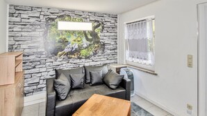 Ein Wohnzimmer mit Wandgemälde aus Stein, einer schwarzen Ledersofa mit Kissen, einem Holztisch und einem Fenster mit weißem Vorhang.