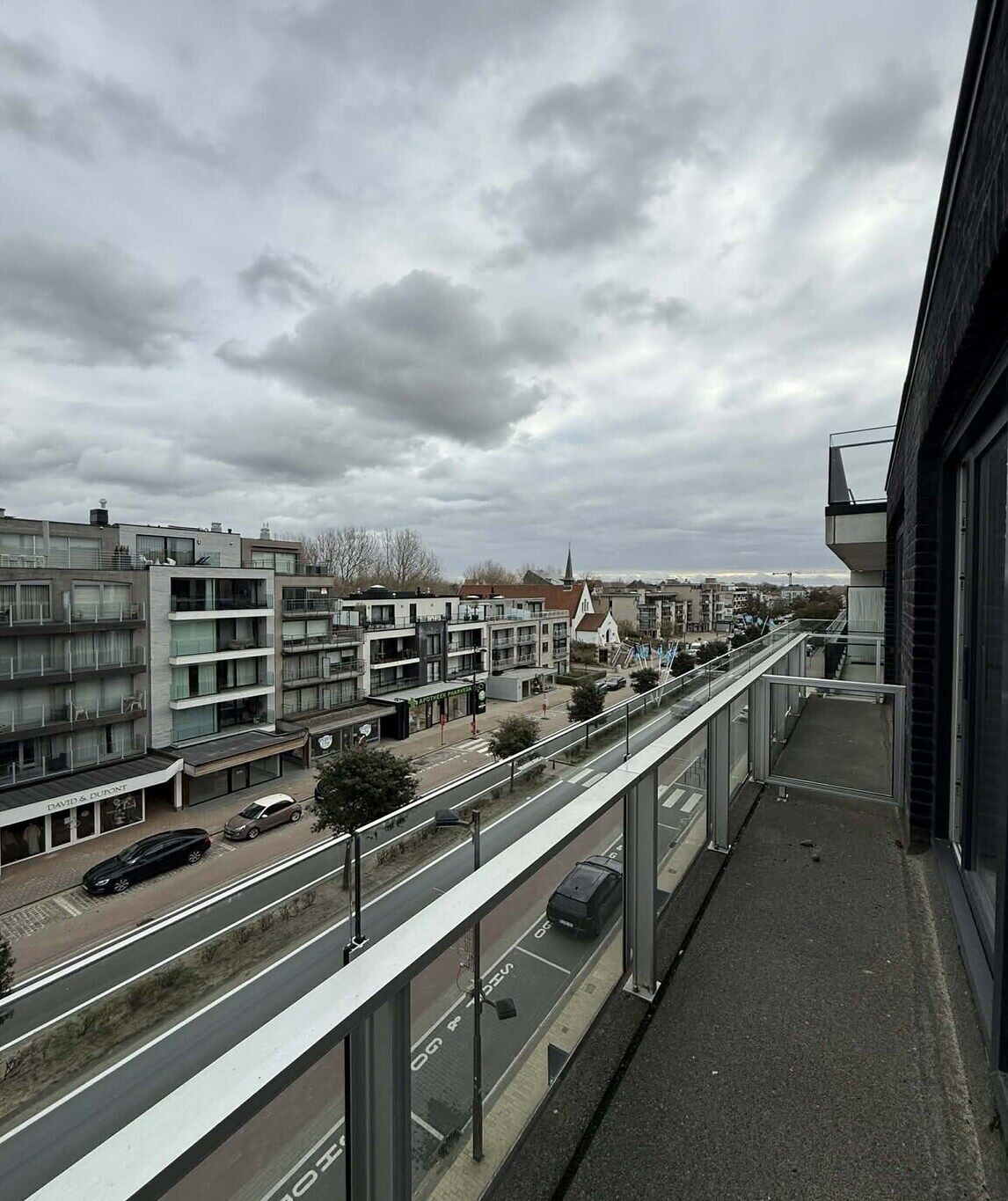 Ein modernes Gebäude mit einem Glasbalkon mit Blick auf eine Straße mit Autos und anderen Gebäuden.