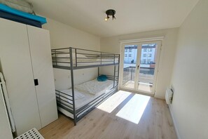 Een slaapzaal met stapelbedden, een garderobe, een radiator en een raam met uitzicht op gebouwen.