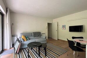 A living room with a sofa, two small tables, a TV, and a dining area. - Couples Retreat Near the Dunes (OOSTDUINKERKE)