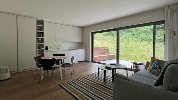 Un interior modern amb zona de menjador, cuina i un gran finestral corredís que dona a un espai exterior.