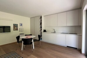 A modern kitchen with white cabinets, a built-in stove, and a dining area with a round table and chairs. - Couples Retreat Near the Dunes (OOSTDUINKERKE)