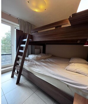 Ein Stockbett mit Holzlade, ein Fenster mit Vorhängen und eine Heizung.