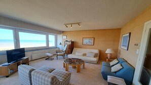 Uma sala de estar com televisão, sofás, uma mesa de centro e vista para a praia.