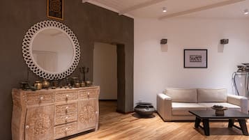 Una sala de estar moderna con piso de madera, un sofá color beige, una mesa de centro negra y un mueble de madera decorativo con objetos de latón.