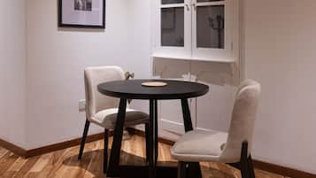 Una habitación con una mesa redonda y dos sillas, un cuadro enmarcado en la pared, y un aparador con puertas de vidrio.