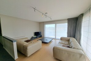 Ein modernes Wohnzimmer mit zwei Sofas, einem Couchtisch, einem Flachbildfernseher und einem großen Fenster mit Vorhängen.